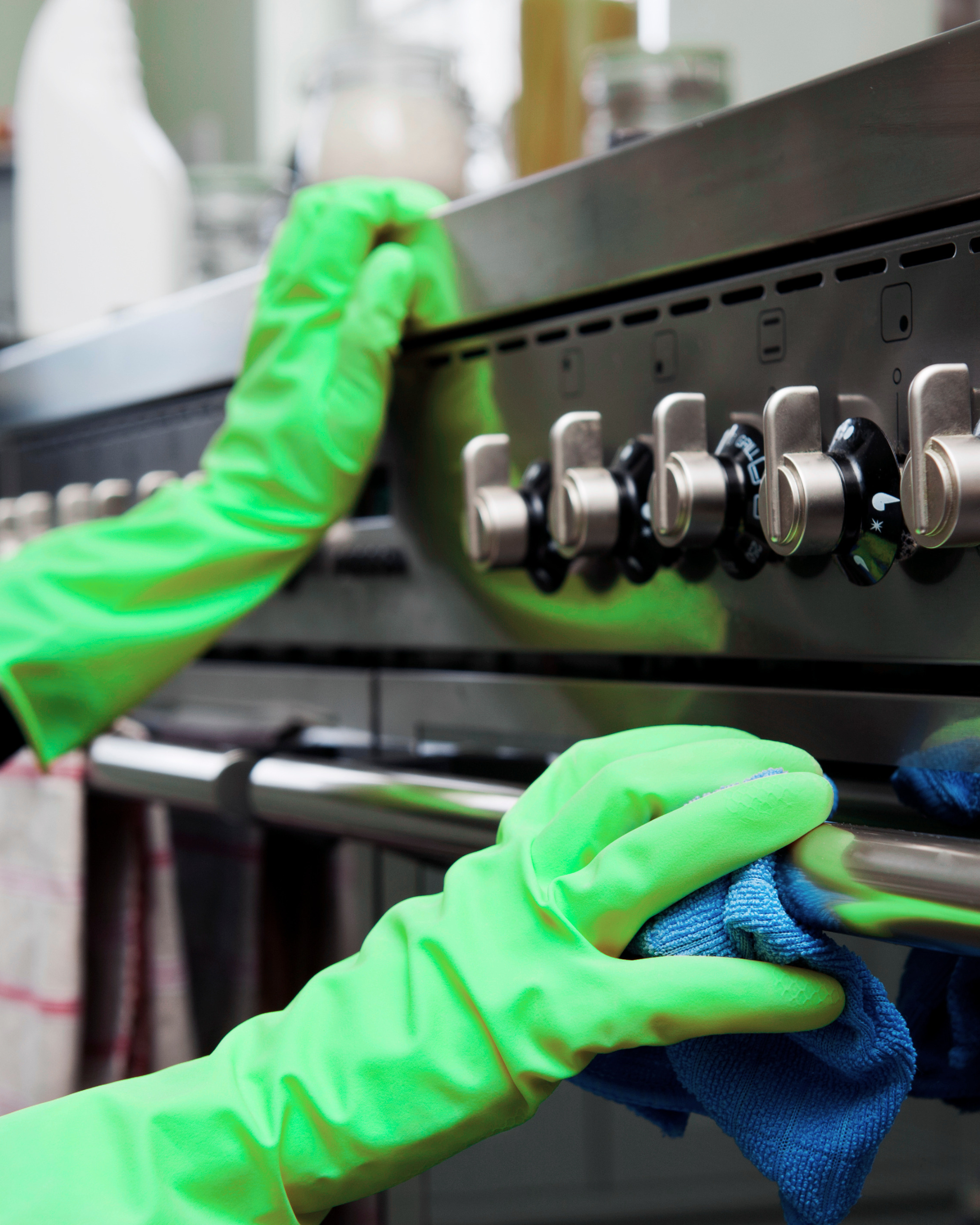 Mik Oy cleaner in green gloves degreasing and wiping down a commercial restaurant stove and knobs in Vantaa, Finland