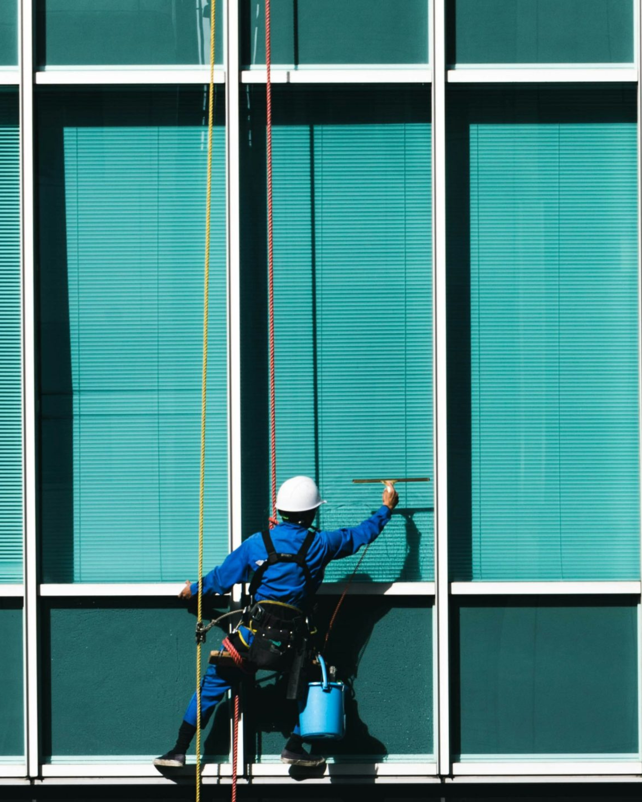 Mik Oy rope access technician in safety harness and helmet cleaning the glass facade of a high-rise commercial building in Vantaa, Finland