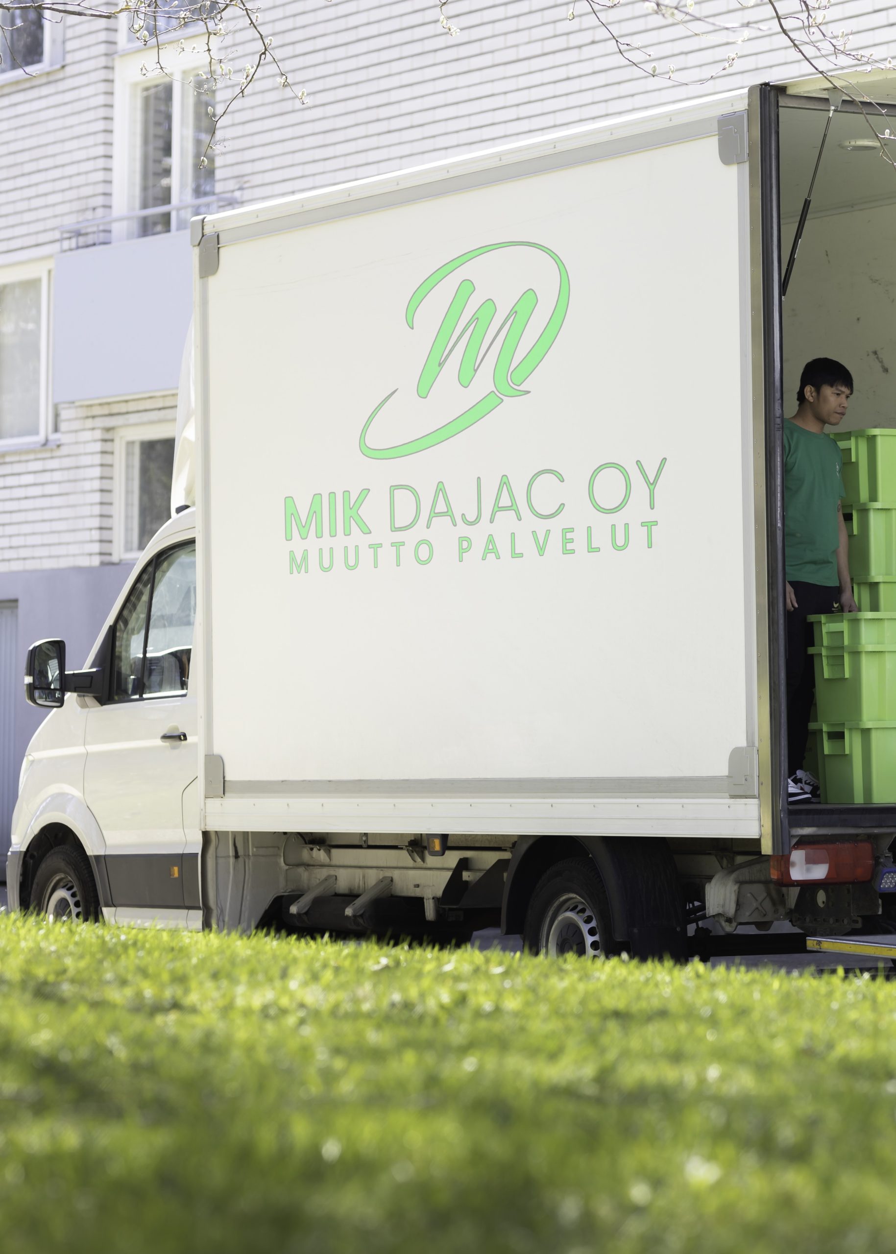 Mik Dajac Oy:n muuttoauto pihalla, työntekijä lastaa muuttolaatikoita kerrostalon edessä
